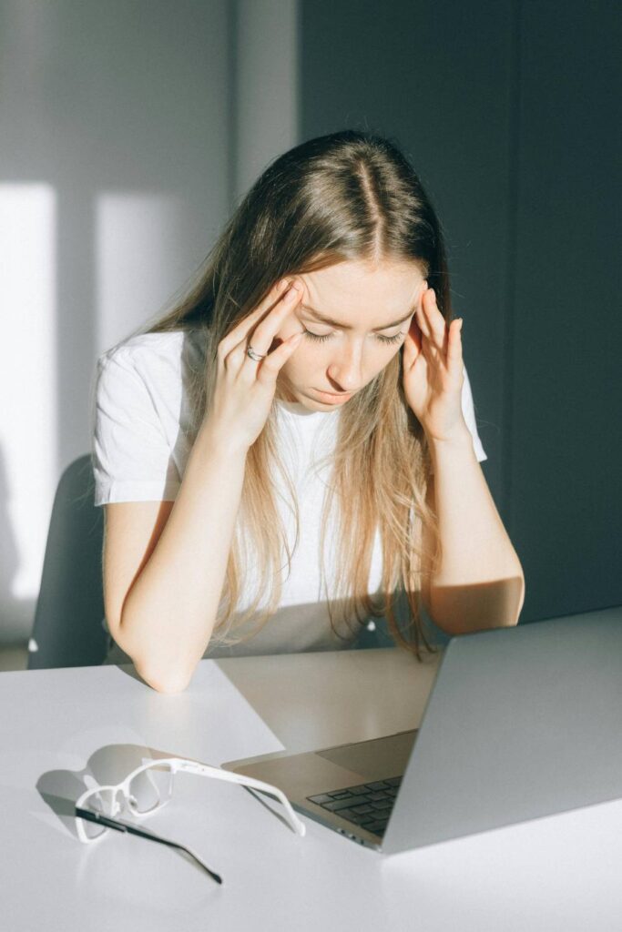 woman with a laptop in front of her, holding her fingers to her temples